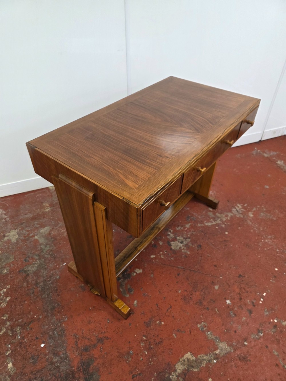 A 1930s Art Deco walnut desk featuring a rectangular top with three drawers, flat slab-style end legs, and a low cross stretcher. View VIII