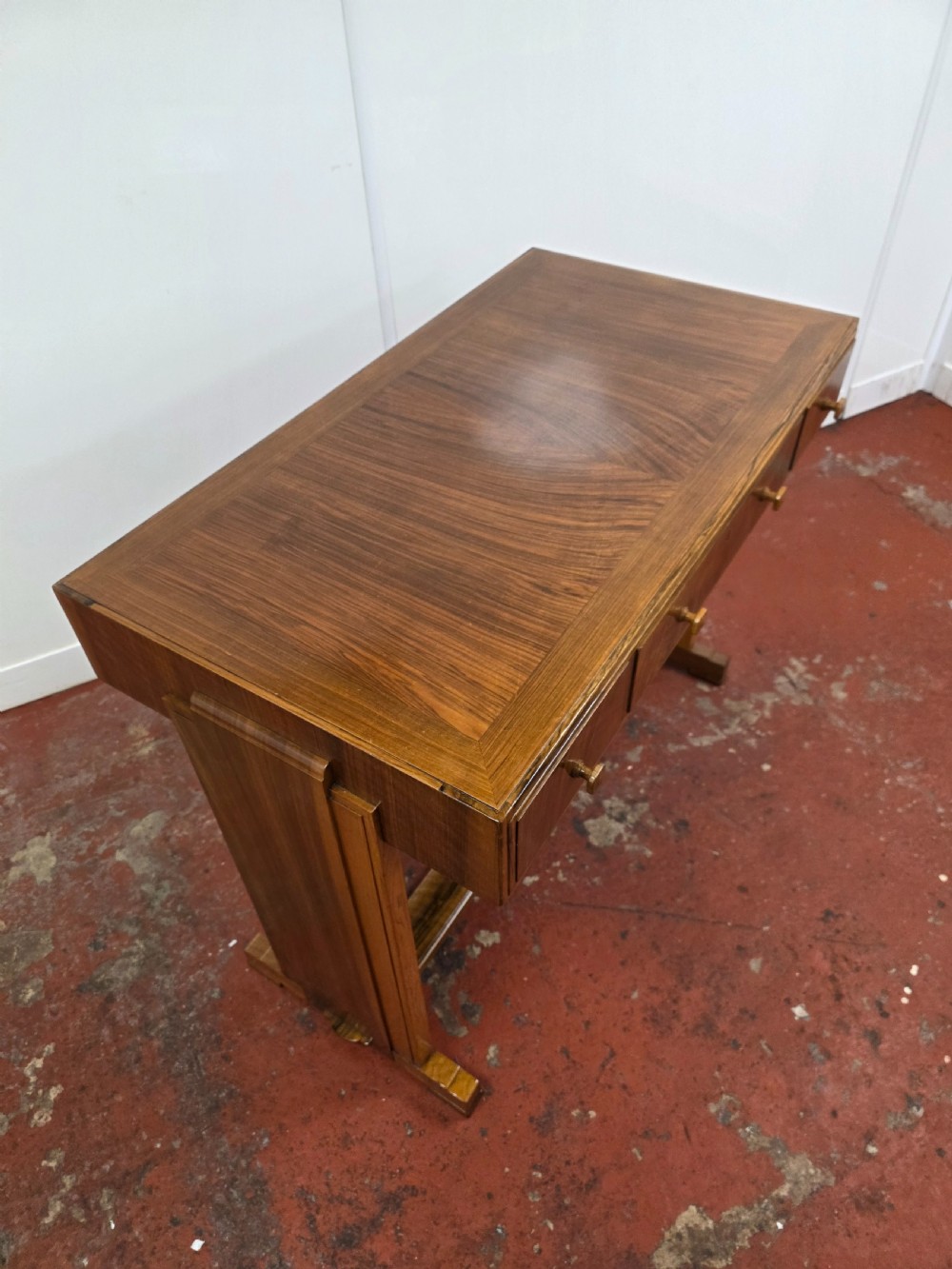 A 1930s Art Deco walnut desk featuring a rectangular top with three drawers, flat slab-style end legs, and a low cross stretcher. View IX