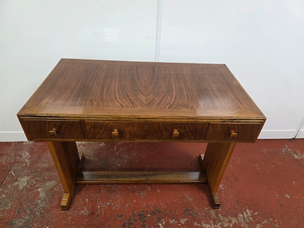 A 1930s Art Deco walnut desk featuring a rectangular top with three drawers, flat slab-style end legs, and a low cross stretcher. View XII
