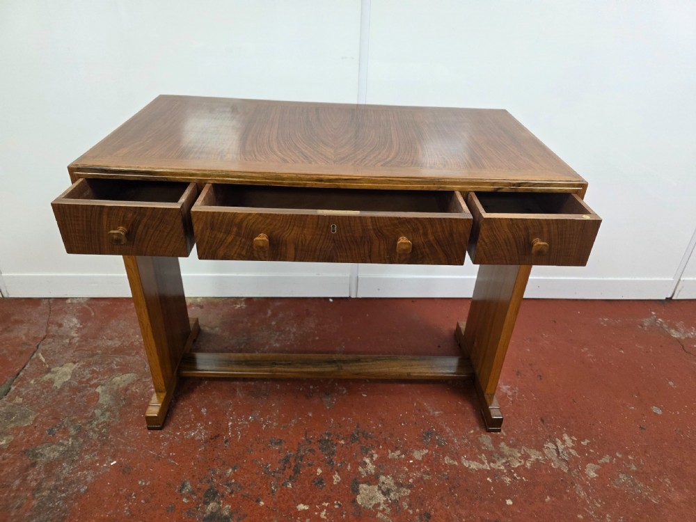 A 1930s Art Deco walnut desk featuring a rectangular top with three drawers, flat slab-style end legs, and a low cross stretcher. View XIII