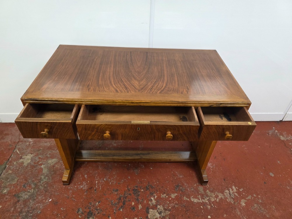 A 1930s Art Deco walnut desk featuring a rectangular top with three drawers, flat slab-style end legs, and a low cross stretcher. View XIV
