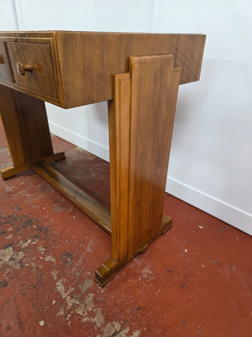 A 1930s Art Deco walnut desk featuring a rectangular top with three drawers, flat slab-style end legs, and a low cross stretcher. View XV