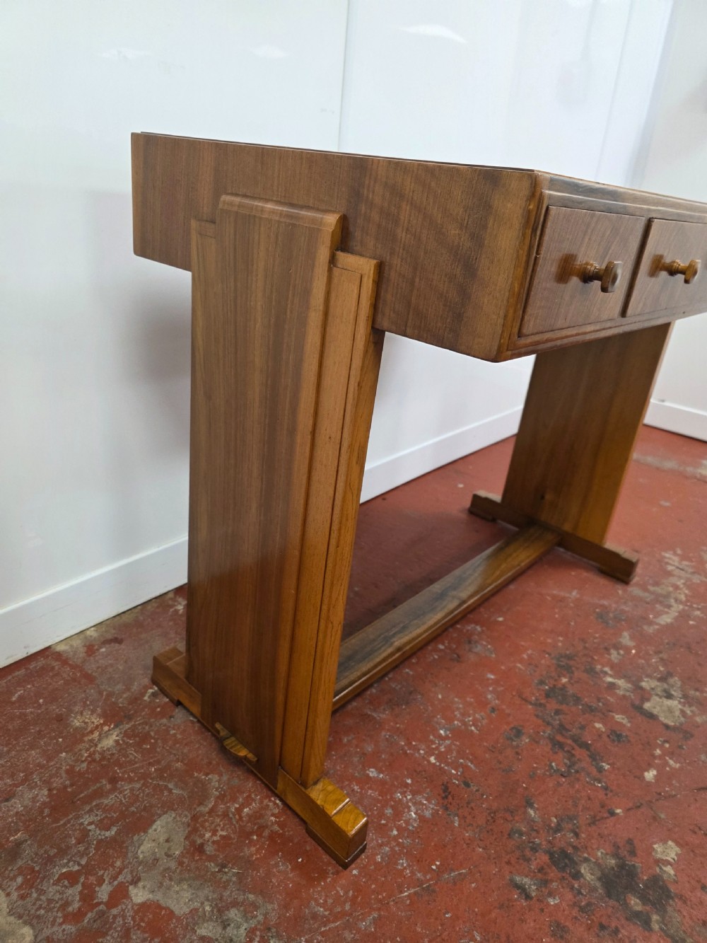 A 1930s Art Deco walnut desk featuring a rectangular top with three drawers, flat slab-style end legs, and a low cross stretcher. View XVI