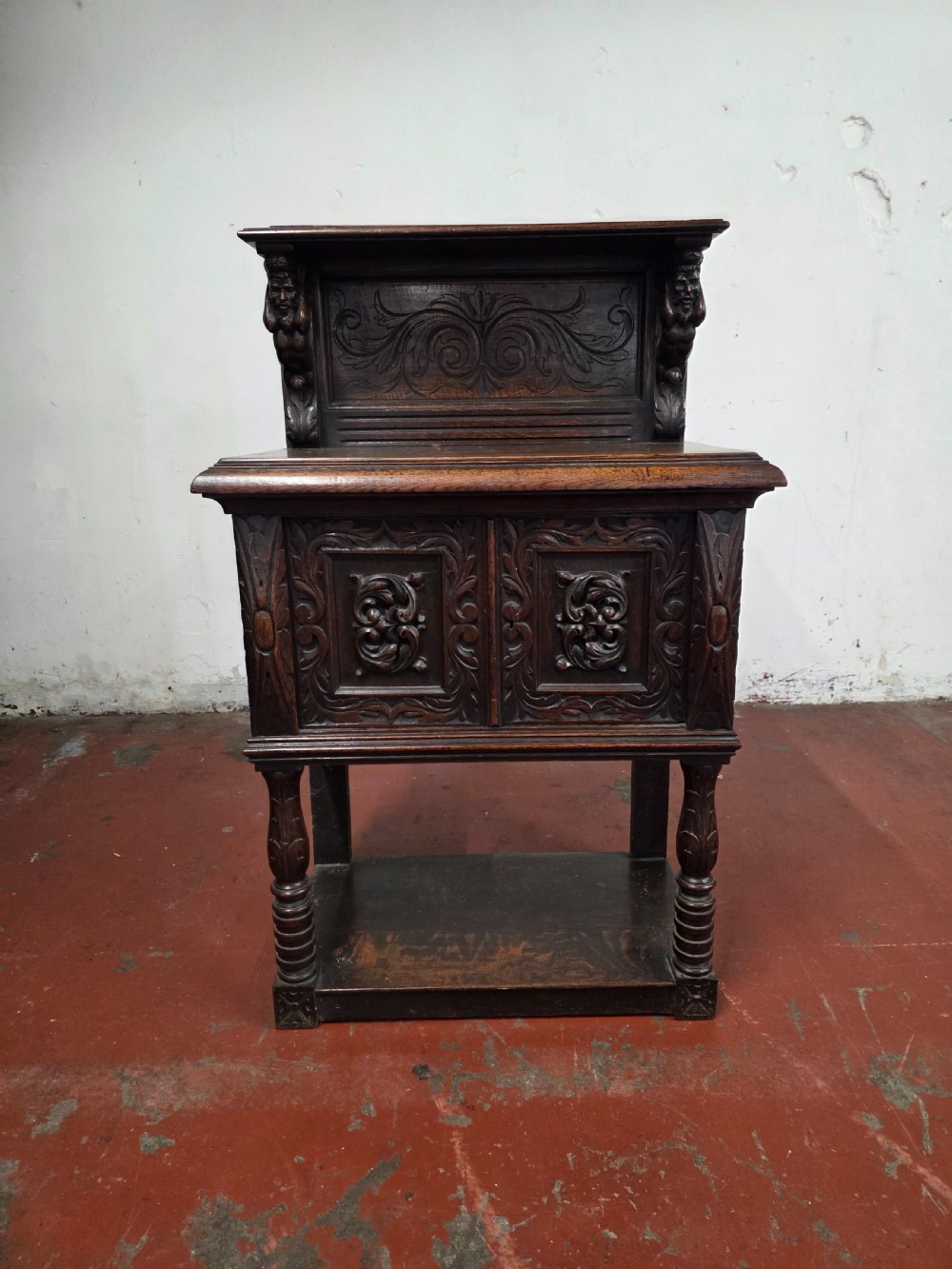A dark brown late Victorian carved oak buffet featuring fielded panels, figural corbels, a tiered plate rack, and a lower undertier shelf.