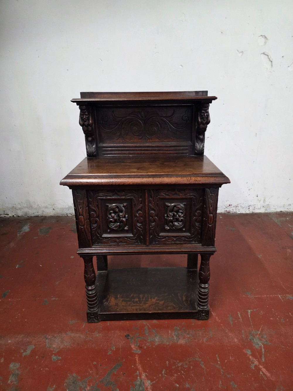 A dark brown late Victorian carved oak buffet featuring fielded panels, figural corbels, a tiered plate rack, and a lower undertier shelf. View II