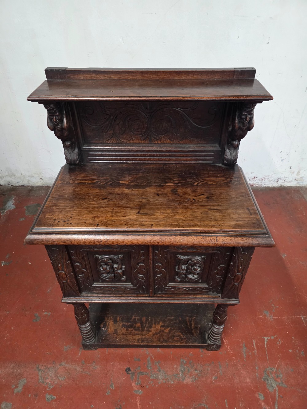 A dark brown late Victorian carved oak buffet featuring fielded panels, figural corbels, a tiered plate rack, and a lower undertier shelf. View V