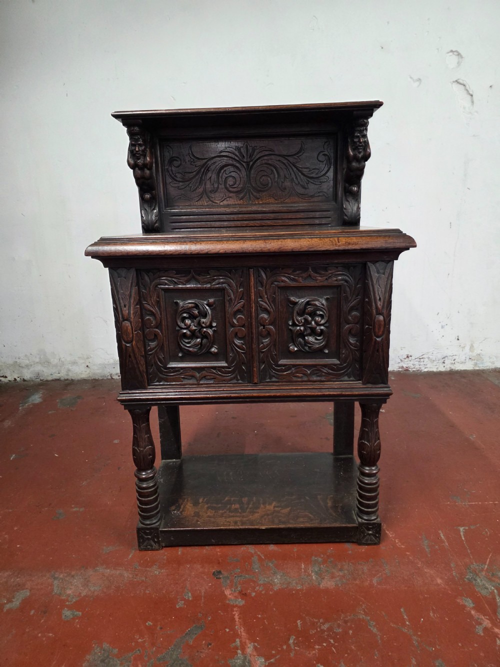 A dark brown late Victorian carved oak buffet featuring fielded panels, figural corbels, a tiered plate rack, and a lower undertier shelf. View VI