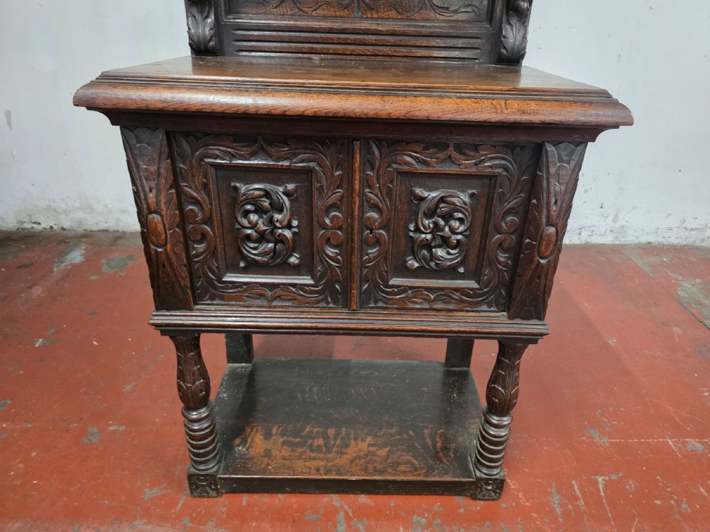 A dark brown late Victorian carved oak buffet featuring fielded panels, figural corbels, a tiered plate rack, and a lower undertier shelf. View IX