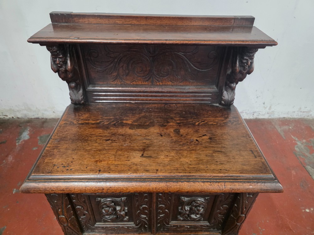 A dark brown late Victorian carved oak buffet featuring fielded panels, figural corbels, a tiered plate rack, and a lower undertier shelf. View XII