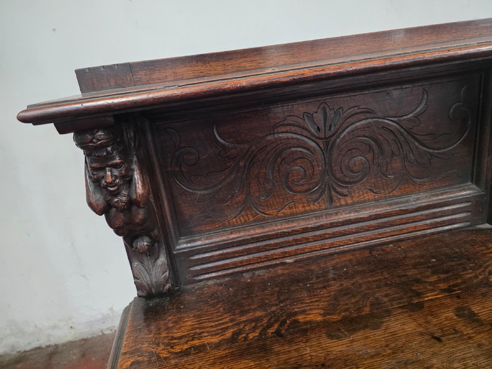 A dark brown late Victorian carved oak buffet featuring fielded panels, figural corbels, a tiered plate rack, and a lower undertier shelf. View XIII