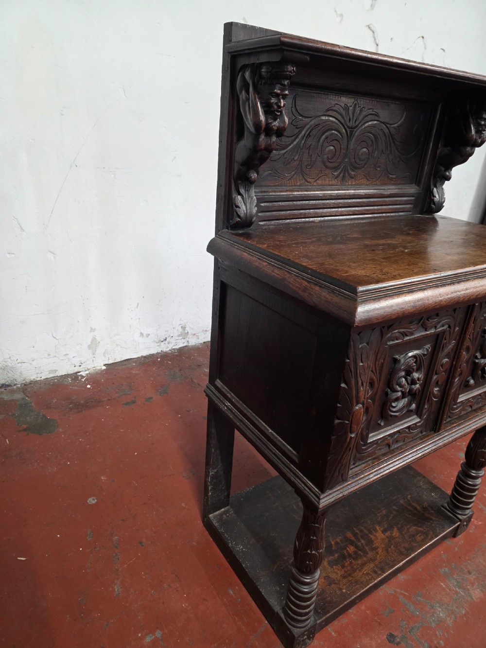 A dark brown late Victorian carved oak buffet featuring fielded panels, figural corbels, a tiered plate rack, and a lower undertier shelf. View XV