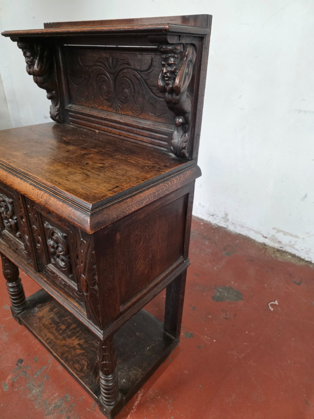 A dark brown late Victorian carved oak buffet featuring fielded panels, figural corbels, a tiered plate rack, and a lower undertier shelf. View XVI