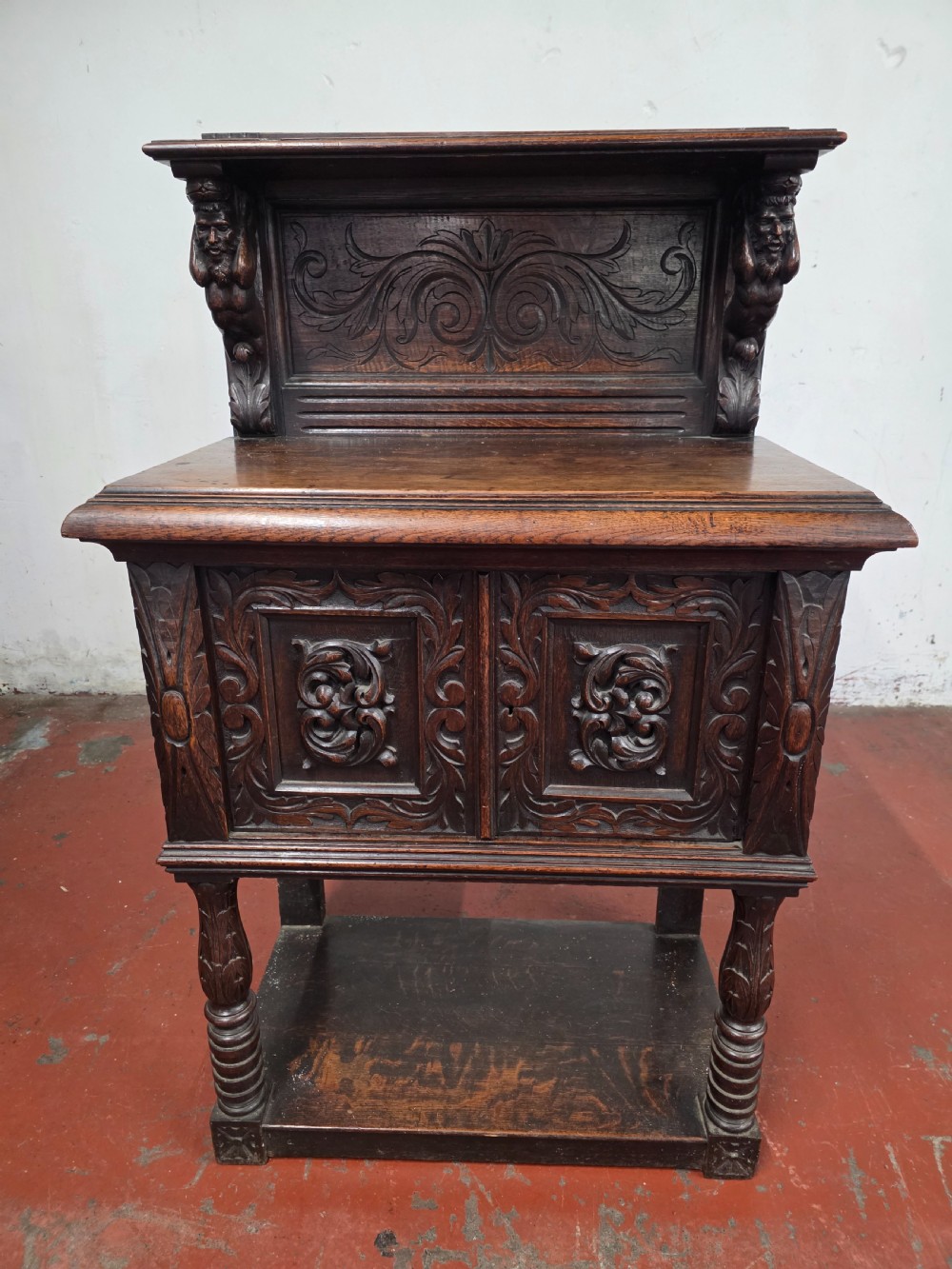 A dark brown late Victorian carved oak buffet featuring fielded panels, figural corbels, a tiered plate rack, and a lower undertier shelf. View XVIII