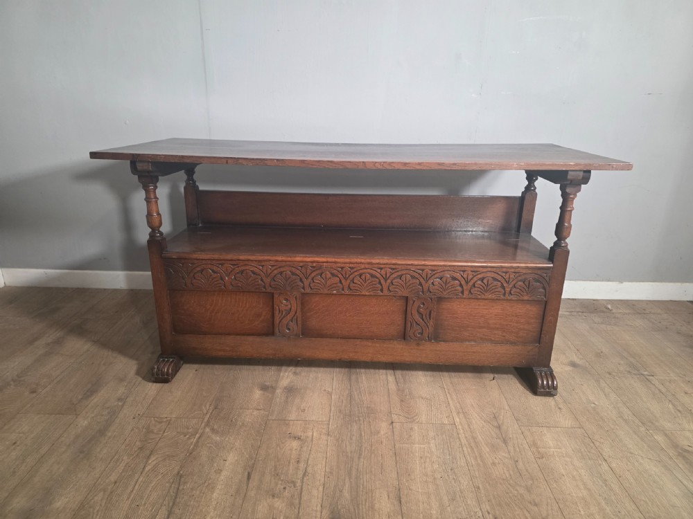A 1920s carved dark oak monks bench featuring a high panelled backrest, turned arm supports, and a lower storage box base. View VIII