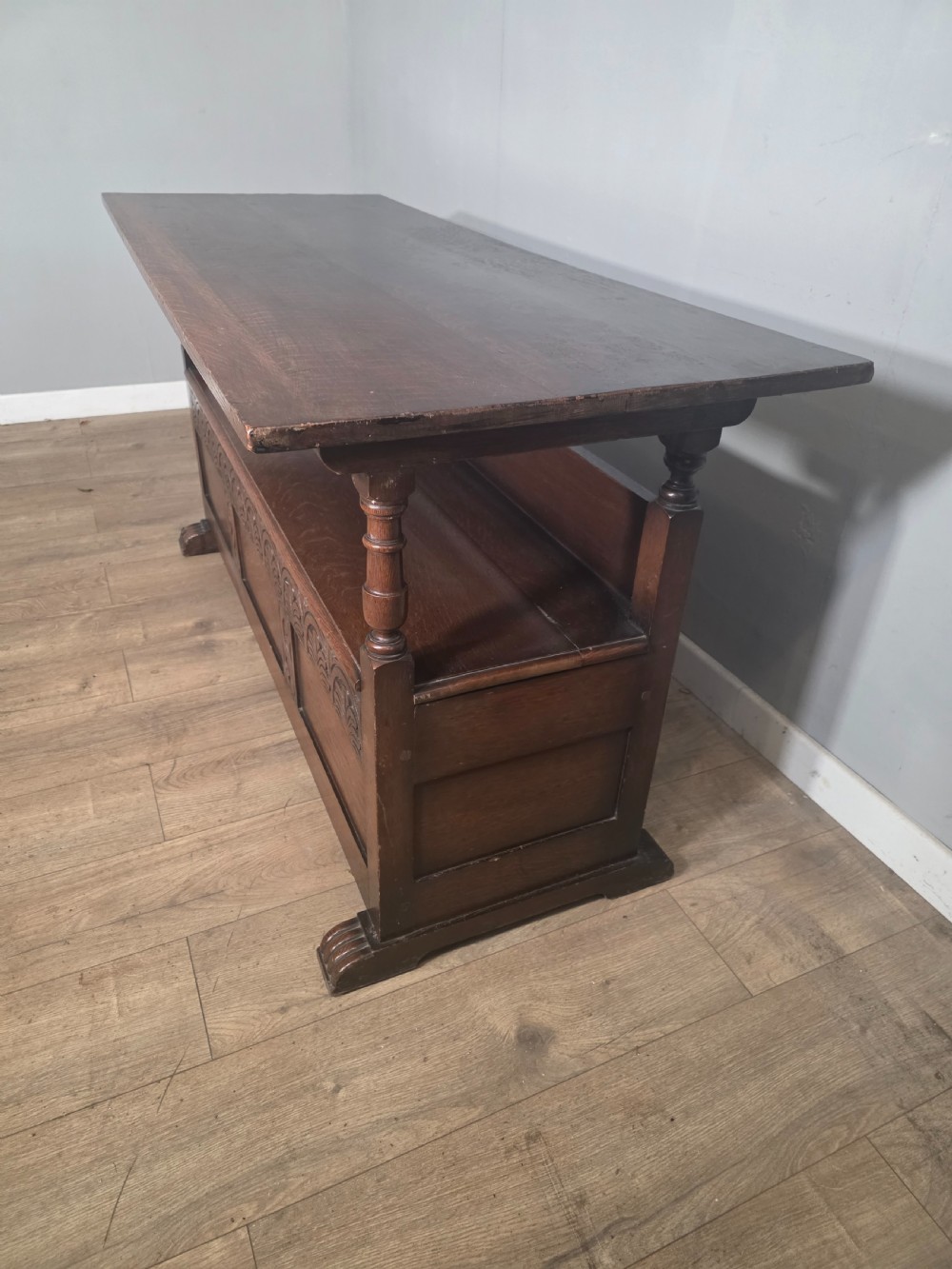 A 1920s carved dark oak monks bench featuring a high panelled backrest, turned arm supports, and a lower storage box base. View XI