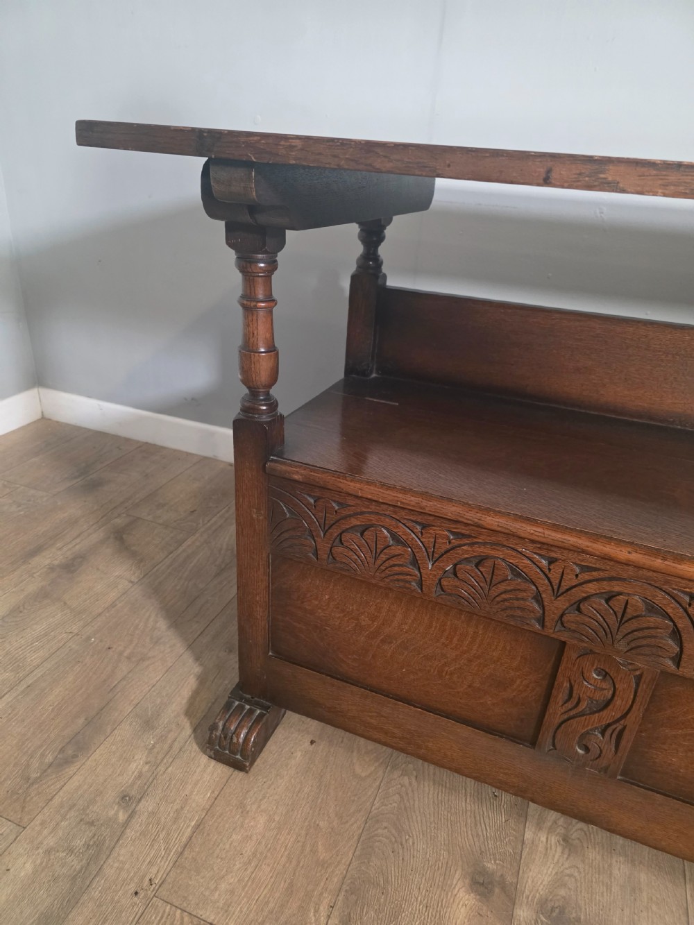 A 1920s carved dark oak monks bench featuring a high panelled backrest, turned arm supports, and a lower storage box base. View XIII