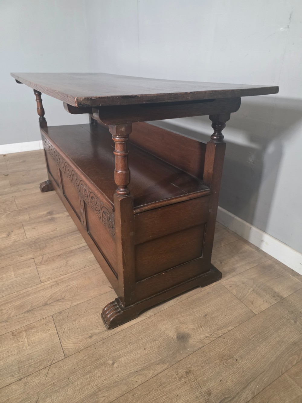 A 1920s carved dark oak monks bench featuring a high panelled backrest, turned arm supports, and a lower storage box base. View XIV