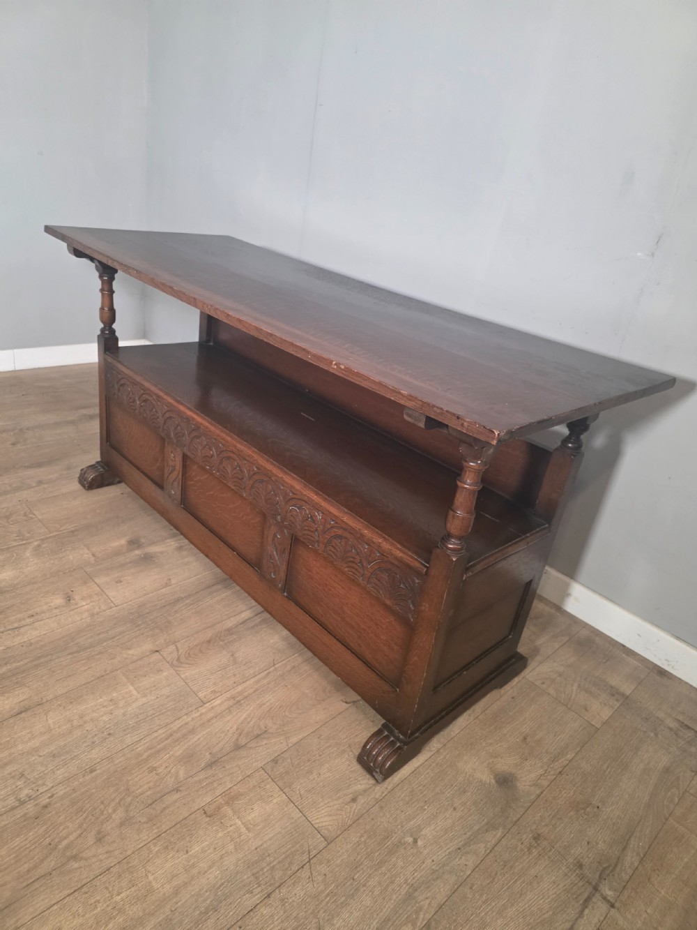 A 1920s carved dark oak monks bench featuring a high panelled backrest, turned arm supports, and a lower storage box base. View XV