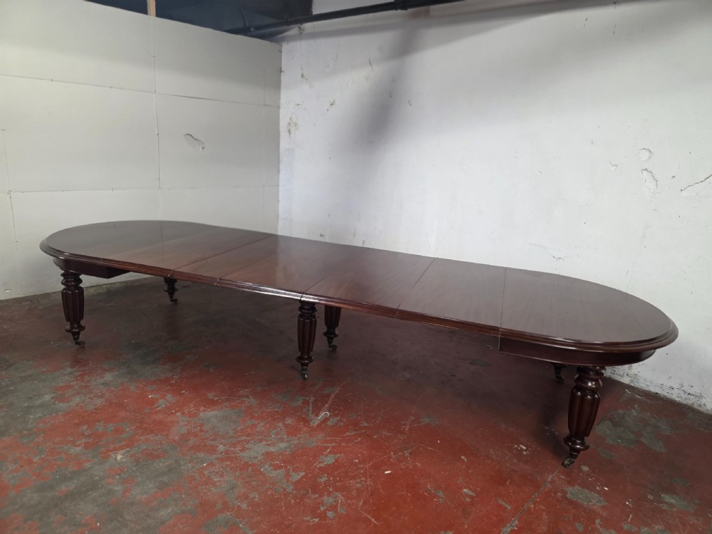 A large William IV mahogany extending banquet dining table featuring rounded ends, multiple insert leaves, and turned legs on brass castors.
