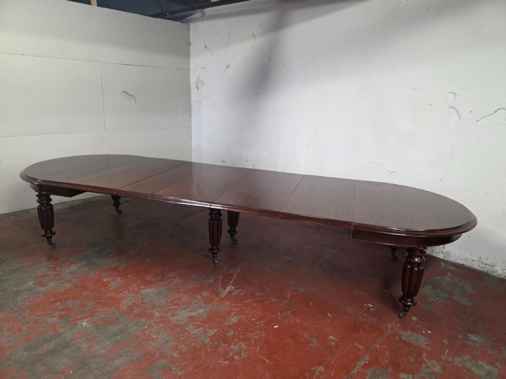 A large William IV mahogany extending banquet dining table featuring rounded ends, multiple insert leaves, and turned legs on brass castors. View II