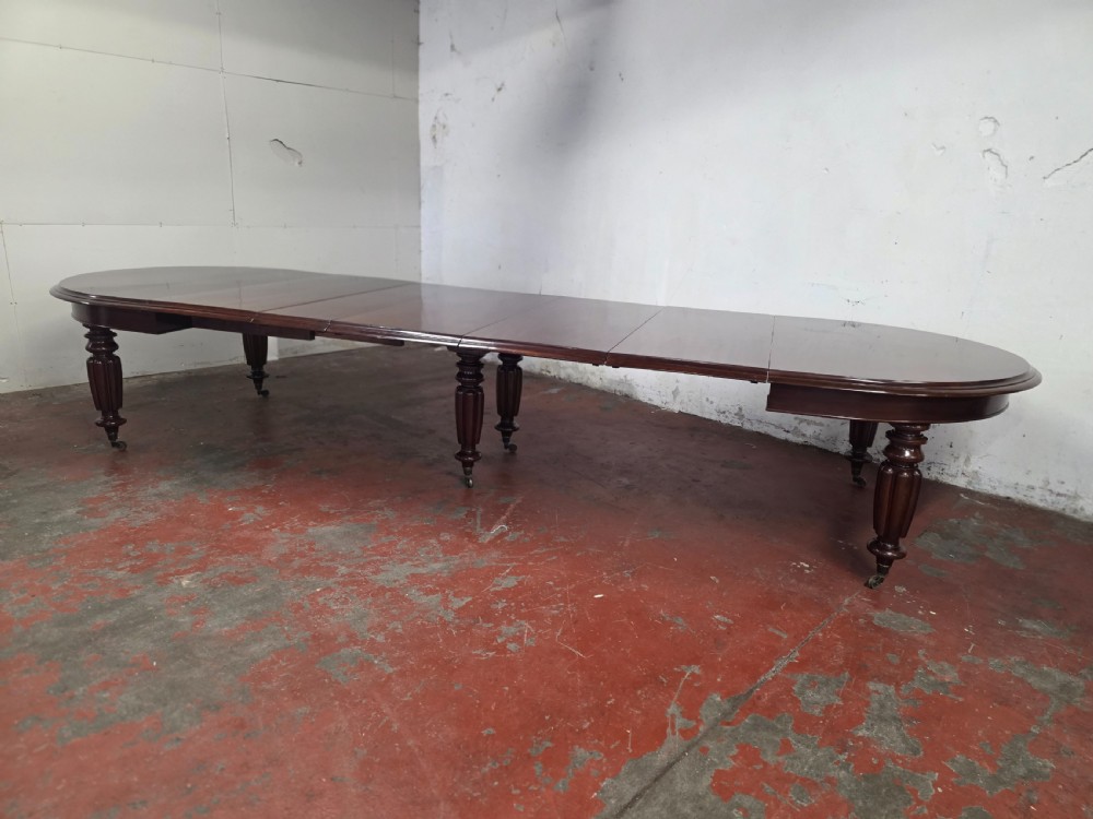 A large William IV mahogany extending banquet dining table featuring rounded ends, multiple insert leaves, and turned legs on brass castors. View III