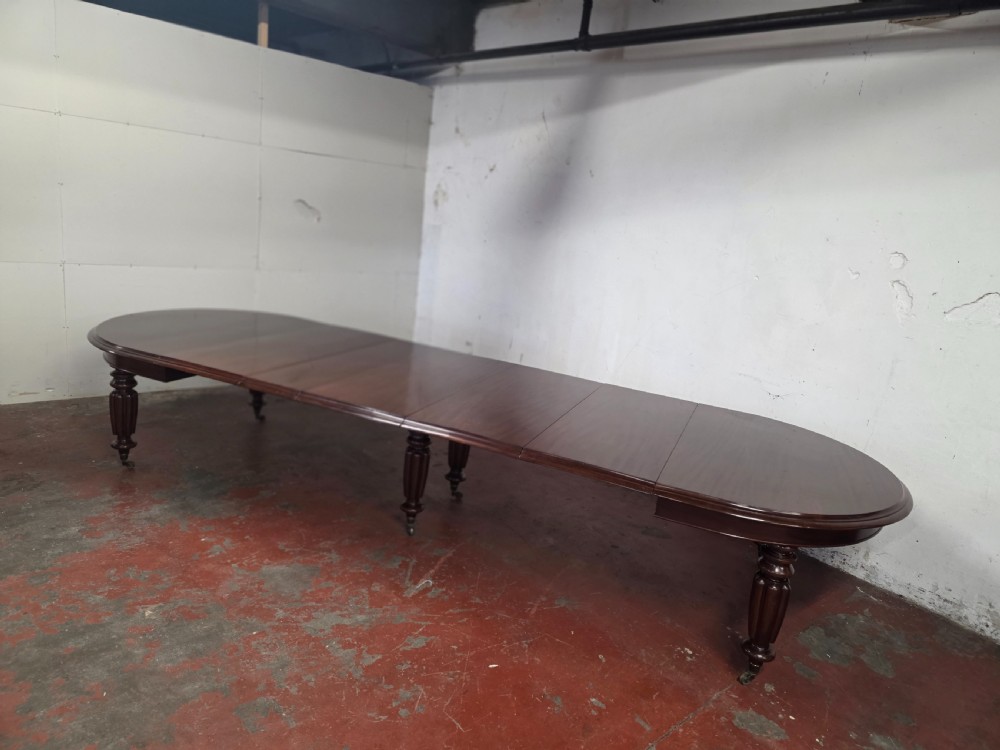 A large William IV mahogany extending banquet dining table featuring rounded ends, multiple insert leaves, and turned legs on brass castors. View IV