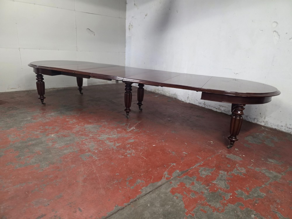 A large William IV mahogany extending banquet dining table featuring rounded ends, multiple insert leaves, and turned legs on brass castors. View V