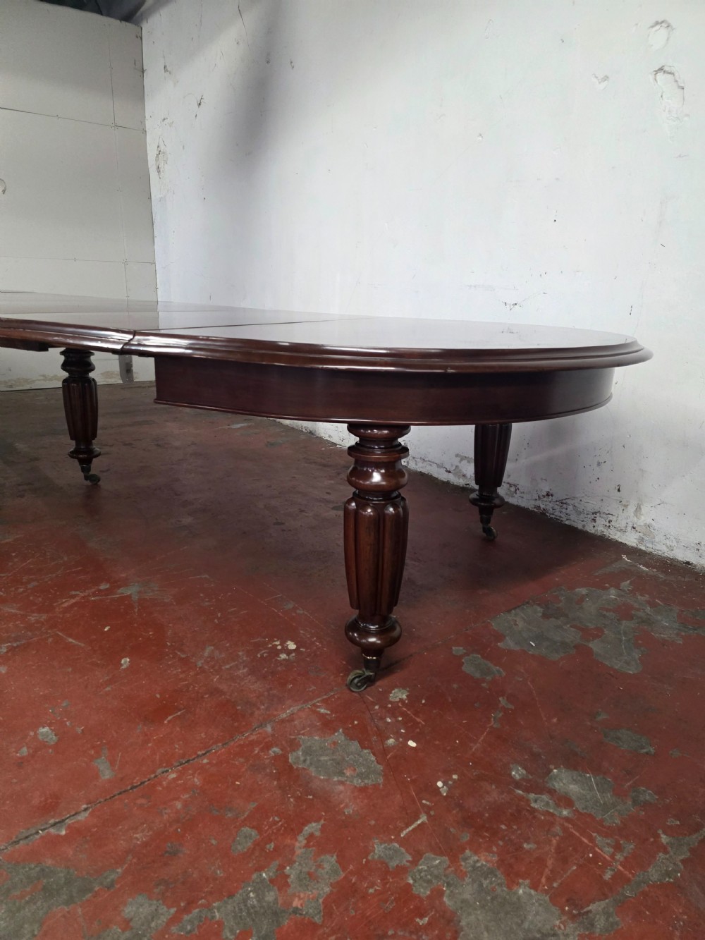 A large William IV mahogany extending banquet dining table featuring rounded ends, multiple insert leaves, and turned legs on brass castors. View VIII