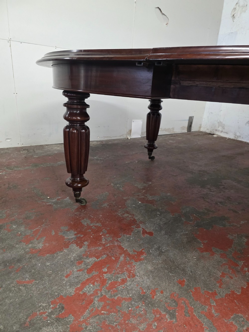 A large William IV mahogany extending banquet dining table featuring rounded ends, multiple insert leaves, and turned legs on brass castors. View IX
