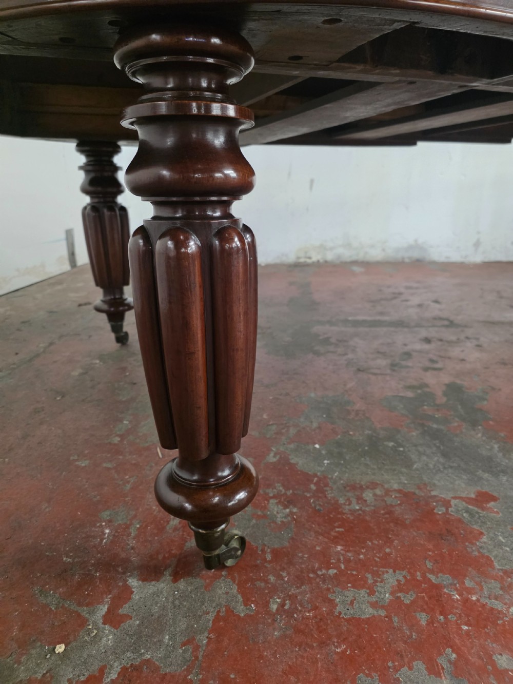 A large William IV mahogany extending banquet dining table featuring rounded ends, multiple insert leaves, and turned legs on brass castors. View XII