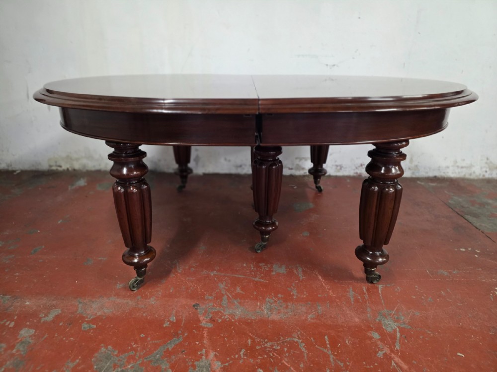 A large William IV mahogany extending banquet dining table featuring rounded ends, multiple insert leaves, and turned legs on brass castors. View XV
