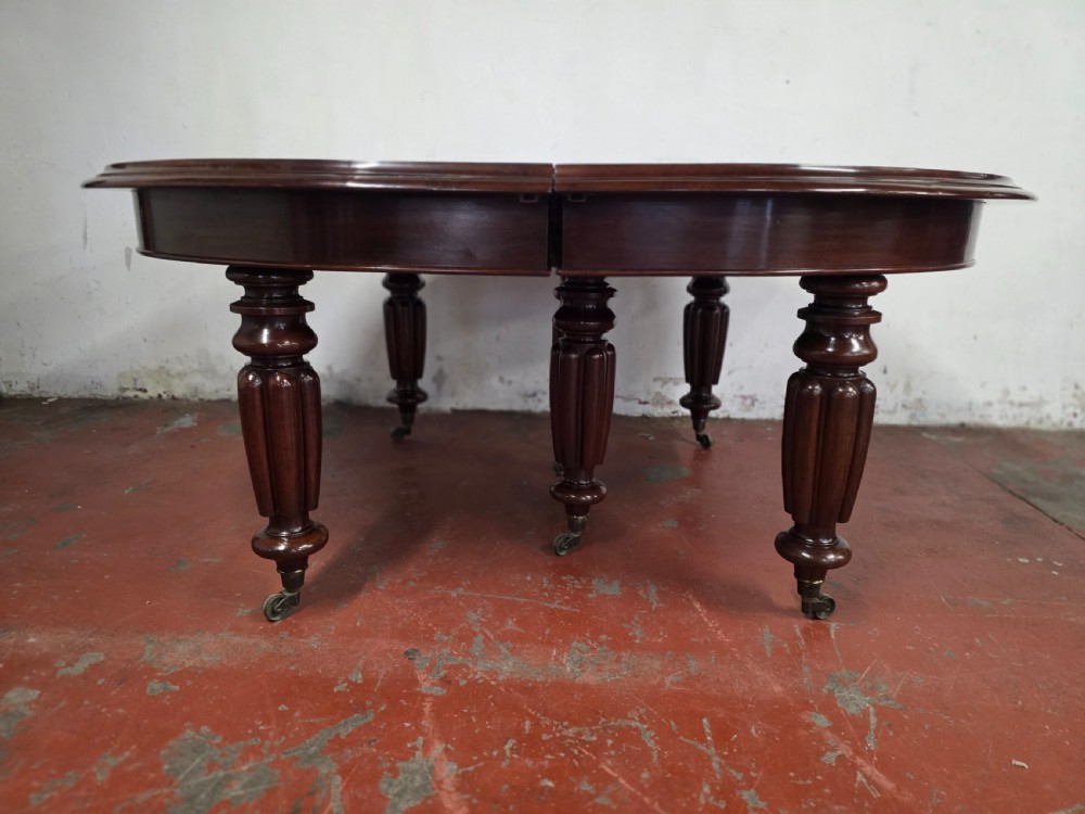 A large William IV mahogany extending banquet dining table featuring rounded ends, multiple insert leaves, and turned legs on brass castors. View XVI