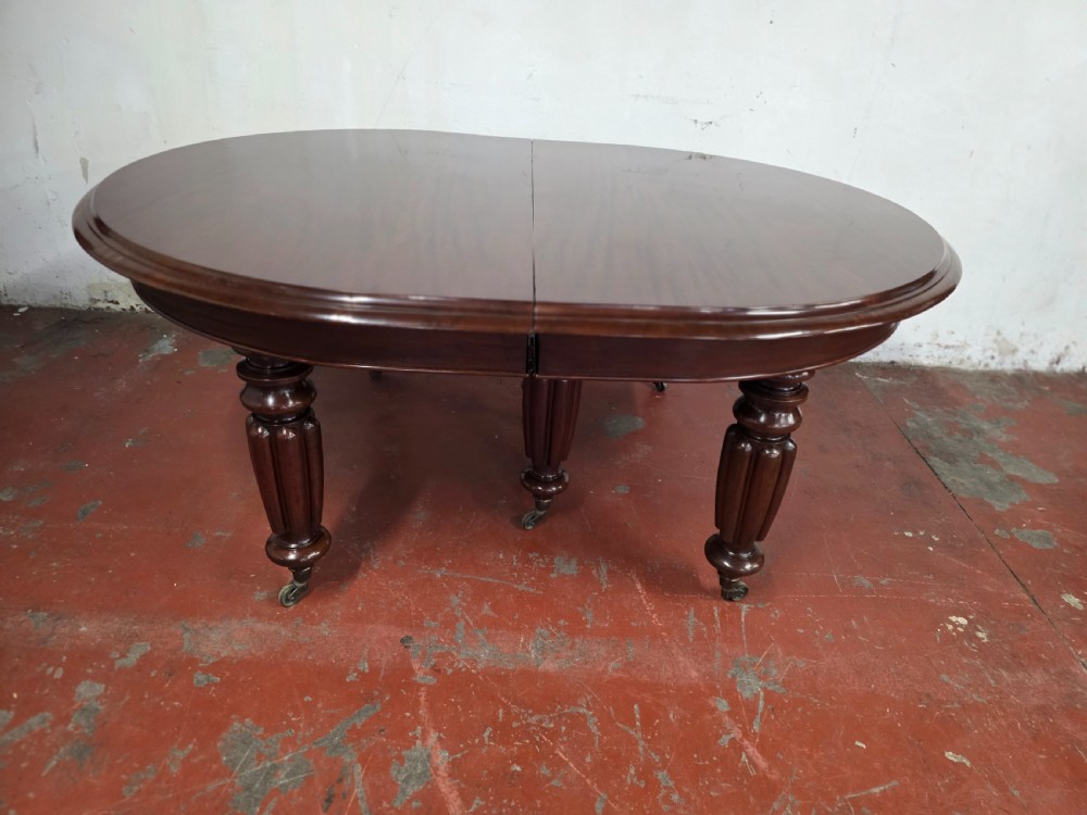 A large William IV mahogany extending banquet dining table featuring rounded ends, multiple insert leaves, and turned legs on brass castors. View XVII