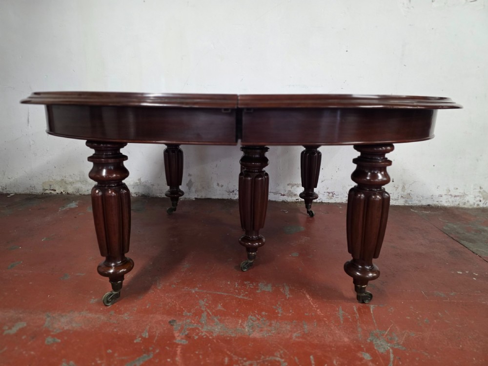 A large William IV mahogany extending banquet dining table featuring rounded ends, multiple insert leaves, and turned legs on brass castors. View XX