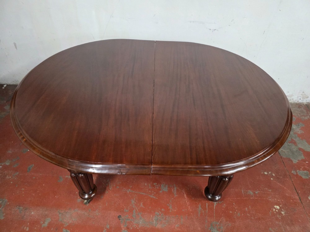 A large William IV mahogany extending banquet dining table featuring rounded ends, multiple insert leaves, and turned legs on brass castors. View XXI