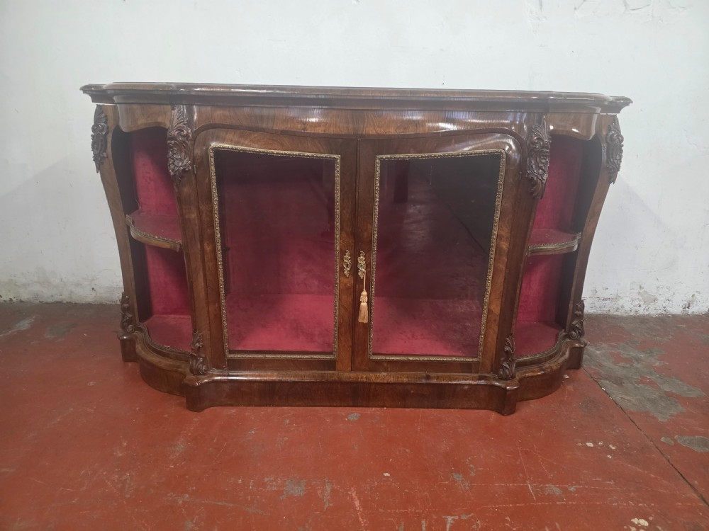A Victorian rosewood credenza featuring central glazed double doors flanked by open curved side shelves with crimson fabric lining.