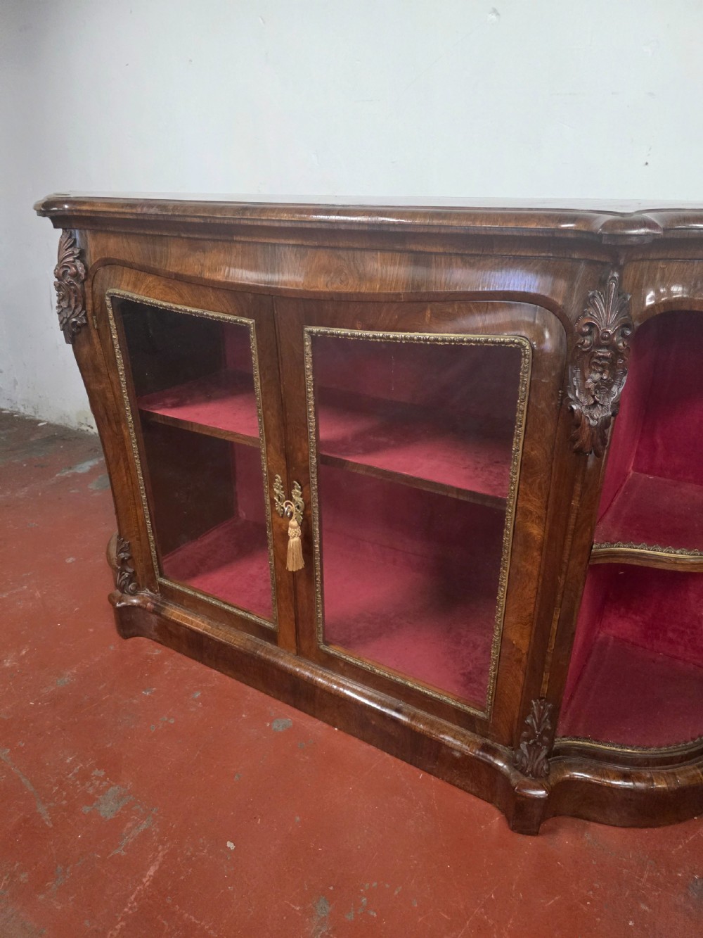 A Victorian rosewood credenza featuring central glazed double doors flanked by open curved side shelves with crimson fabric lining. View XVI