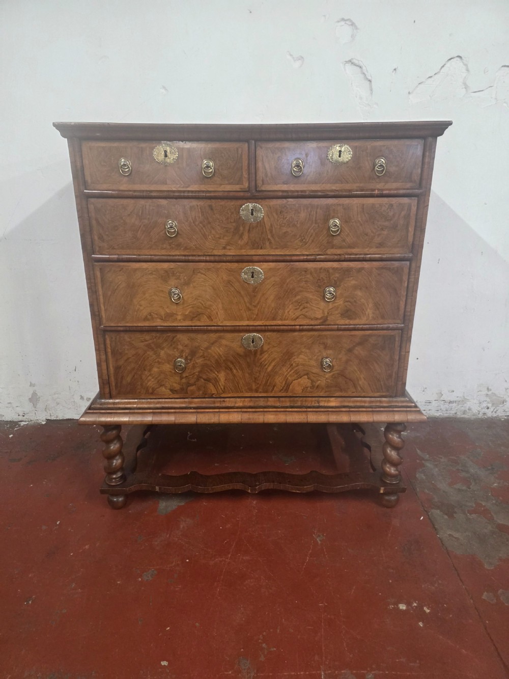 An early 18th-century Queen Anne burr walnut chest on stand featuring multiple graduated drawers with brass handles, resting on a base with barley twist legs and a shaped stretcher.
