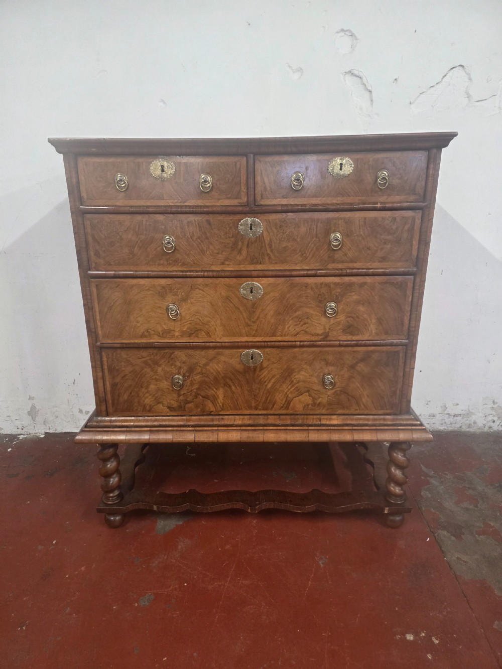 An early 18th-century Queen Anne burr walnut chest on stand featuring multiple graduated drawers with brass handles, resting on a base with barley twist legs and a shaped stretcher. View II