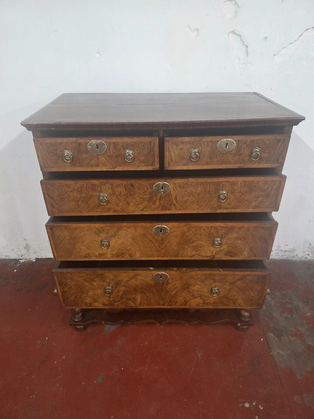An early 18th-century Queen Anne burr walnut chest on stand featuring multiple graduated drawers with brass handles, resting on a base with barley twist legs and a shaped stretcher. View V