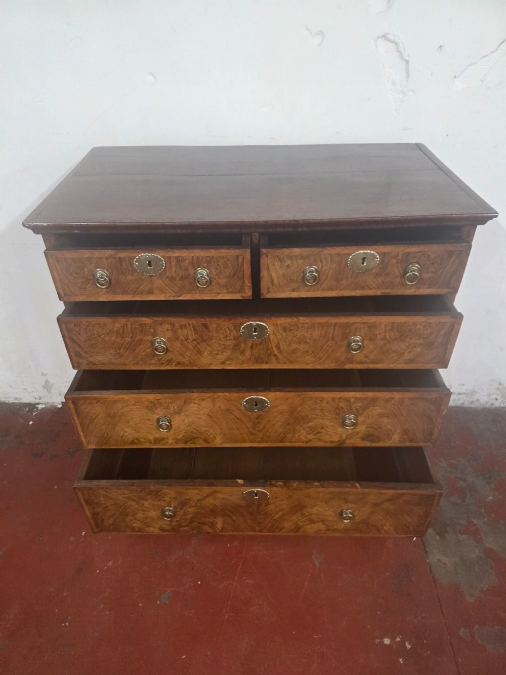 An early 18th-century Queen Anne burr walnut chest on stand featuring multiple graduated drawers with brass handles, resting on a base with barley twist legs and a shaped stretcher. View VI
