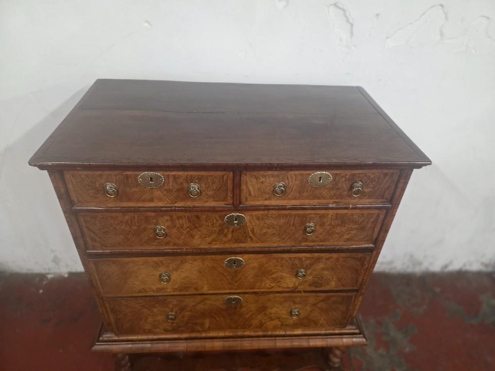 An early 18th-century Queen Anne burr walnut chest on stand featuring multiple graduated drawers with brass handles, resting on a base with barley twist legs and a shaped stretcher. View XII