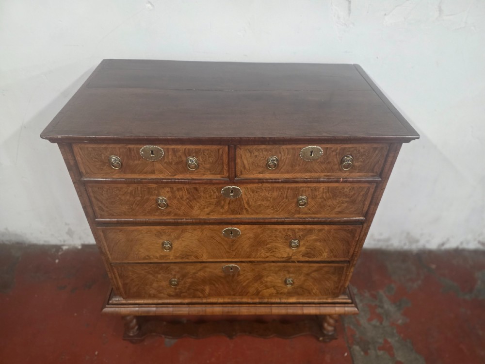 An early 18th-century Queen Anne burr walnut chest on stand featuring multiple graduated drawers with brass handles, resting on a base with barley twist legs and a shaped stretcher. View XIII