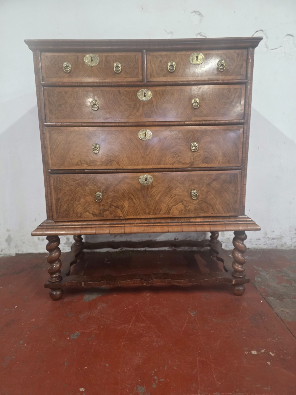 An early 18th-century Queen Anne burr walnut chest on stand featuring multiple graduated drawers with brass handles, resting on a base with barley twist legs and a shaped stretcher. View XIV