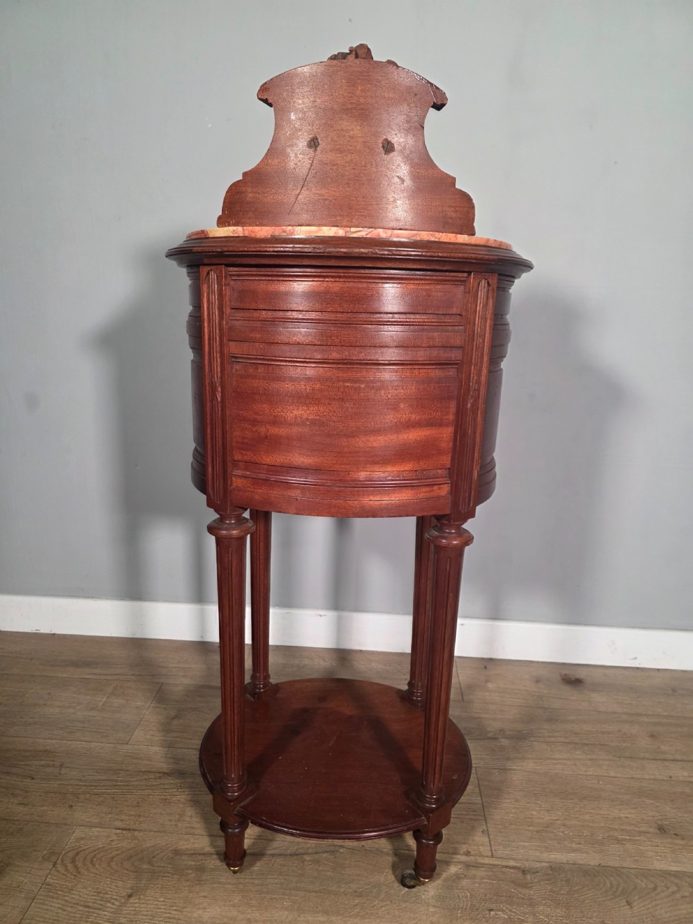 An antique French mahogany bedside cabinet featuring an oval marble top, a carved cresting gallery, a single drawer above a cupboard door, turned fluted legs, and a lower shelf. View X