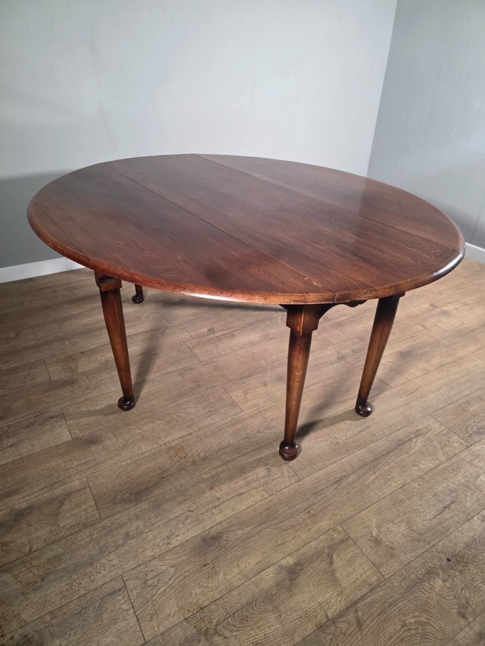 A large oval solid oak drop-leaf wake dining table featuring tapered legs with pad feet. View II