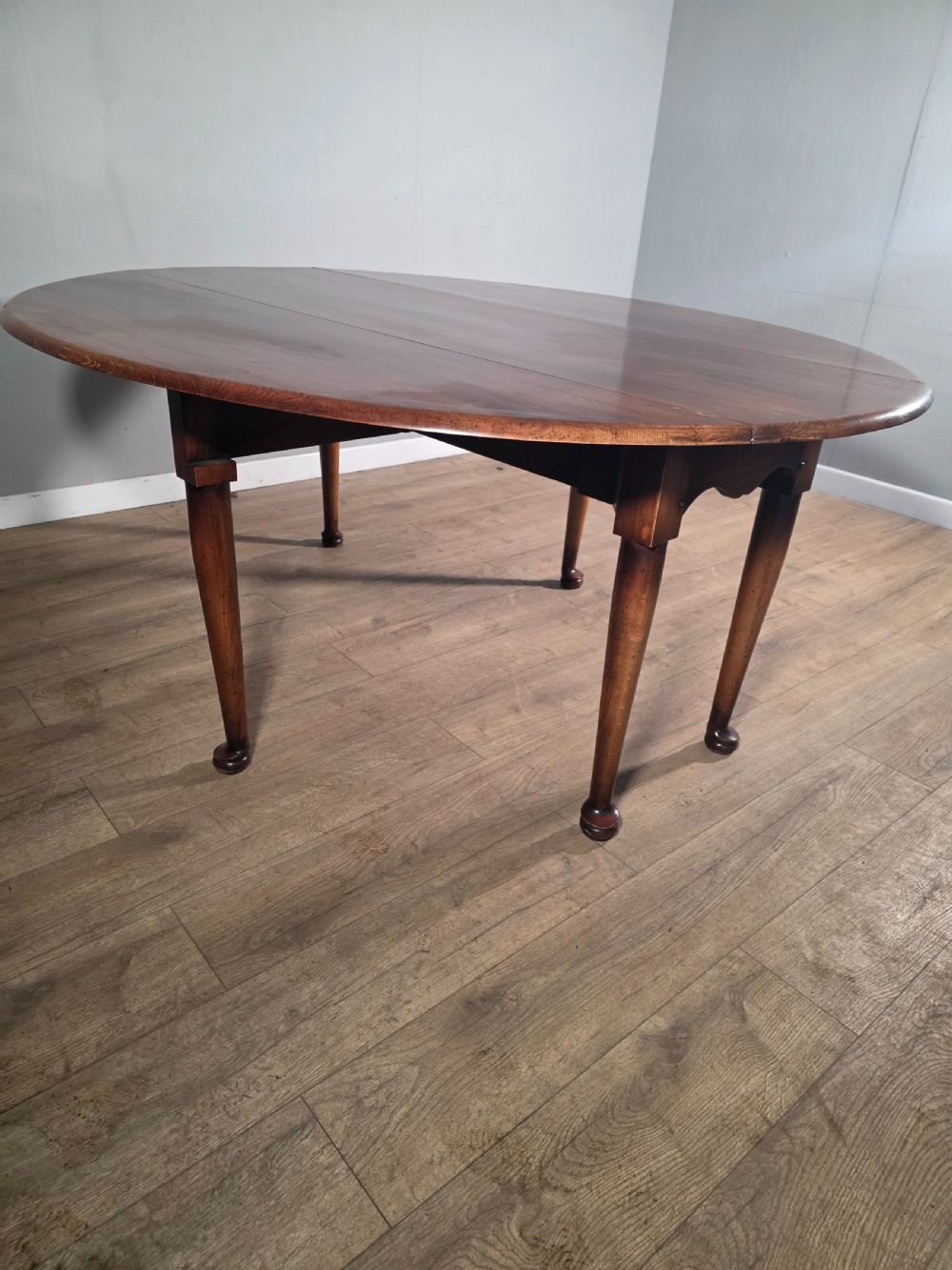 A large oval solid oak drop-leaf wake dining table featuring tapered legs with pad feet. View VI