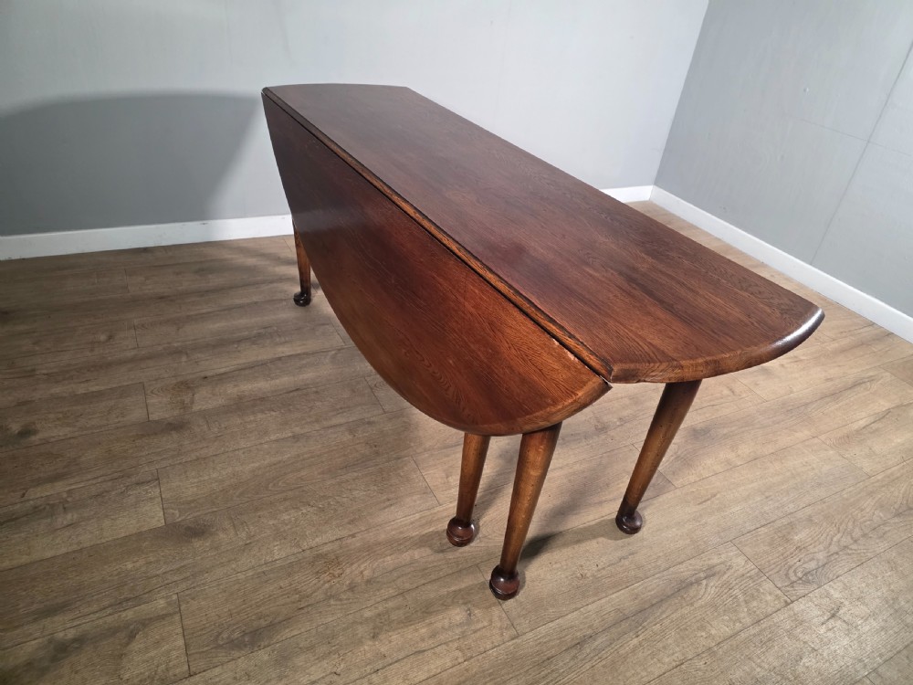 A large oval solid oak drop-leaf wake dining table featuring tapered legs with pad feet. View XIV
