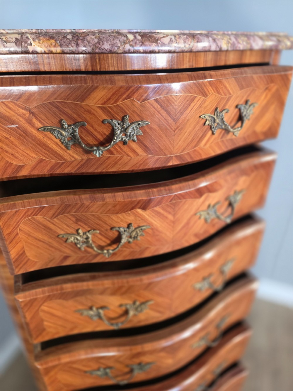 A tall 1930s French semainier chest featuring seven inlaid wood drawers, cast brass handles, a fitted brown marble top, and curved legs. View XIII