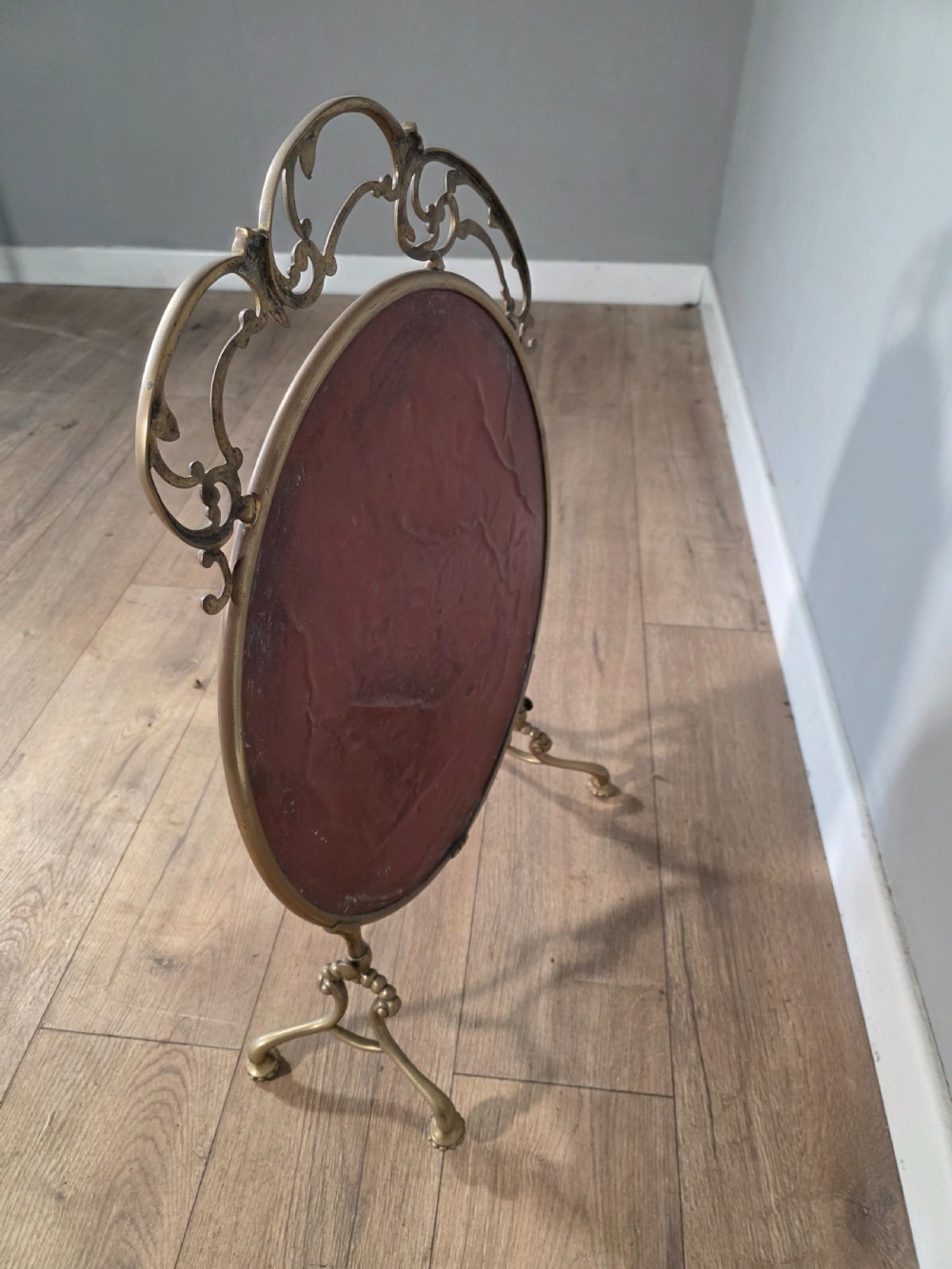An Art Nouveau brass fire screen containing an oval bevelled glass panel engraved with a floral motif, set on splayed brass legs. View VII